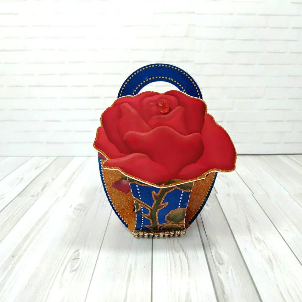 Cestinha personalizada do tema Bela e a Fera com alça em formato de rosa vermelha 3D de papel, corpo em estampa floral azul com borda de trepadeira de rosas e acabamento dourado