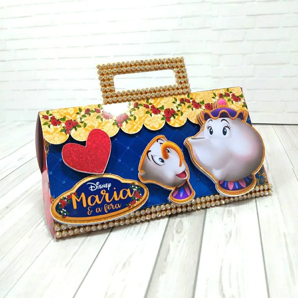 Caixa maletinha com alça revestida de pedraria, em azul-royal com borda de filete dourado floral, ilustrações recortadas do bule de chá e da xícara encantados, coração de glitter vermelho e selo oval com a frase 'Disney Maria & a Fera'