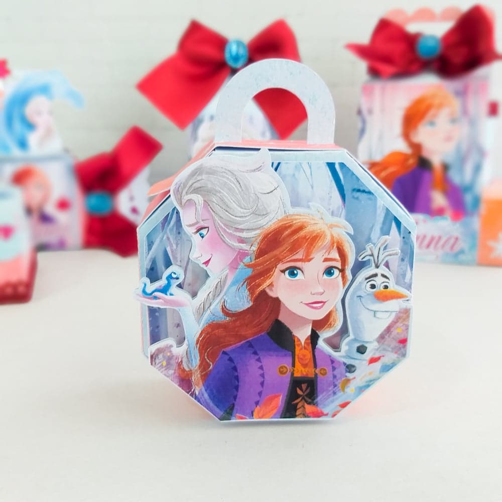 Caixa hexagonal com alça do tema Frozen com Elsa, Anna e Olaf junto de Bruni, a pequena salamandra, coroada com laço de cetim vermelho e gema facetada em tom teal