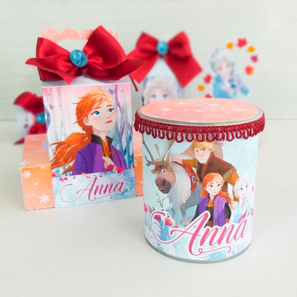 Caixa lata cilíndrica do tema Frozen com trança de tecido ao redor da tampa estampada com flocos de neve rosa, decorada com Kristoff, Sven, Anna e Elsa e o nome 'Anna' em script rosa