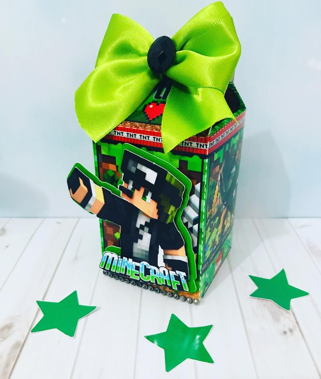 Caixa Milk personalizada no tema Minecraft com laço de cetim verde-limão, botão preto facetado no centro e personagem em estilo pixelado no painel frontal