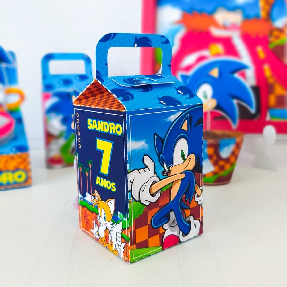 Caixa Milk personalizada no tema Sonic, com fundo azul e padrão repetido da cabeça do personagem, painel frontal xadrez laranja e vermelho e o nome 'SANDRO' com a idade '7 ANOS' em amarelo